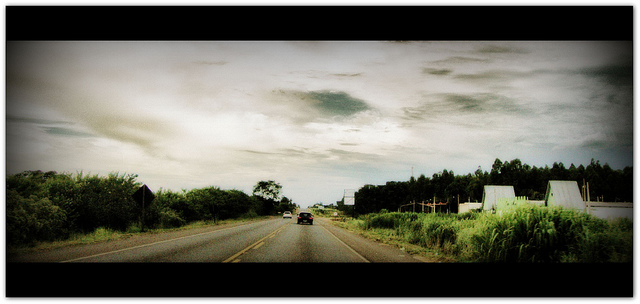 Car on deserted highway below a cloudy sky.