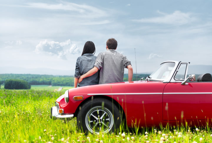 Couple posing by a classic scarlet convertible.