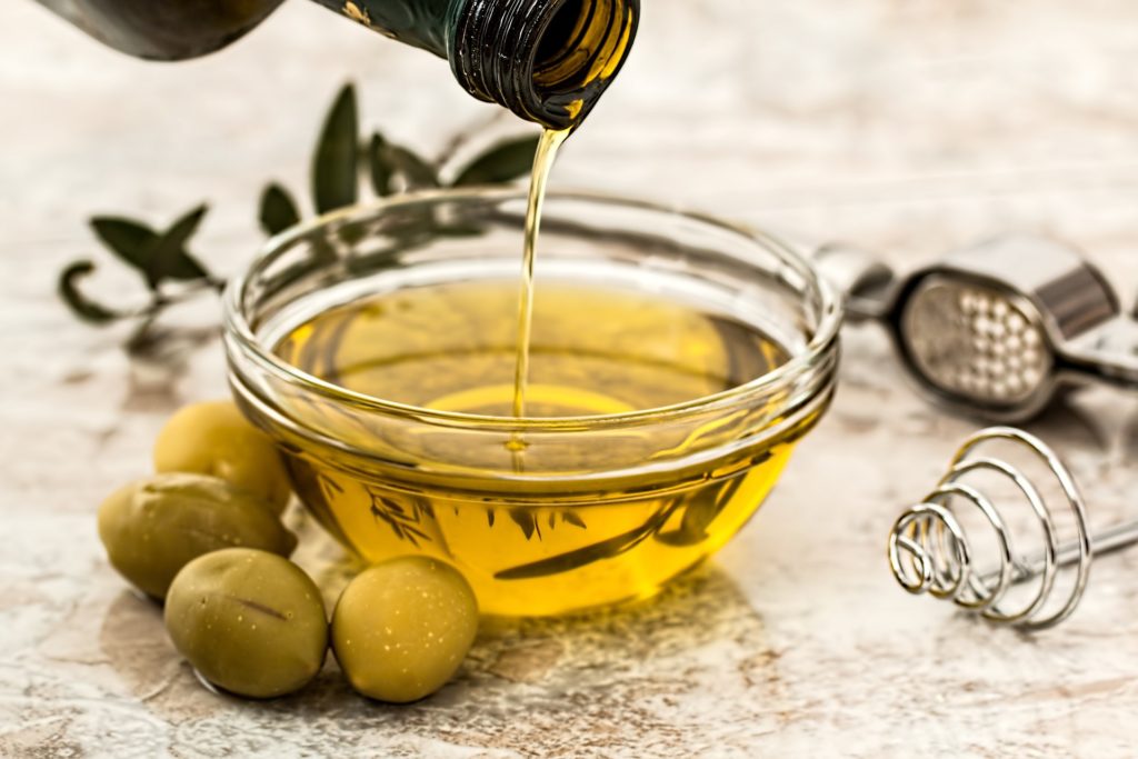 Olive oil pouring into a glass tasting cup, surrounded by olives.