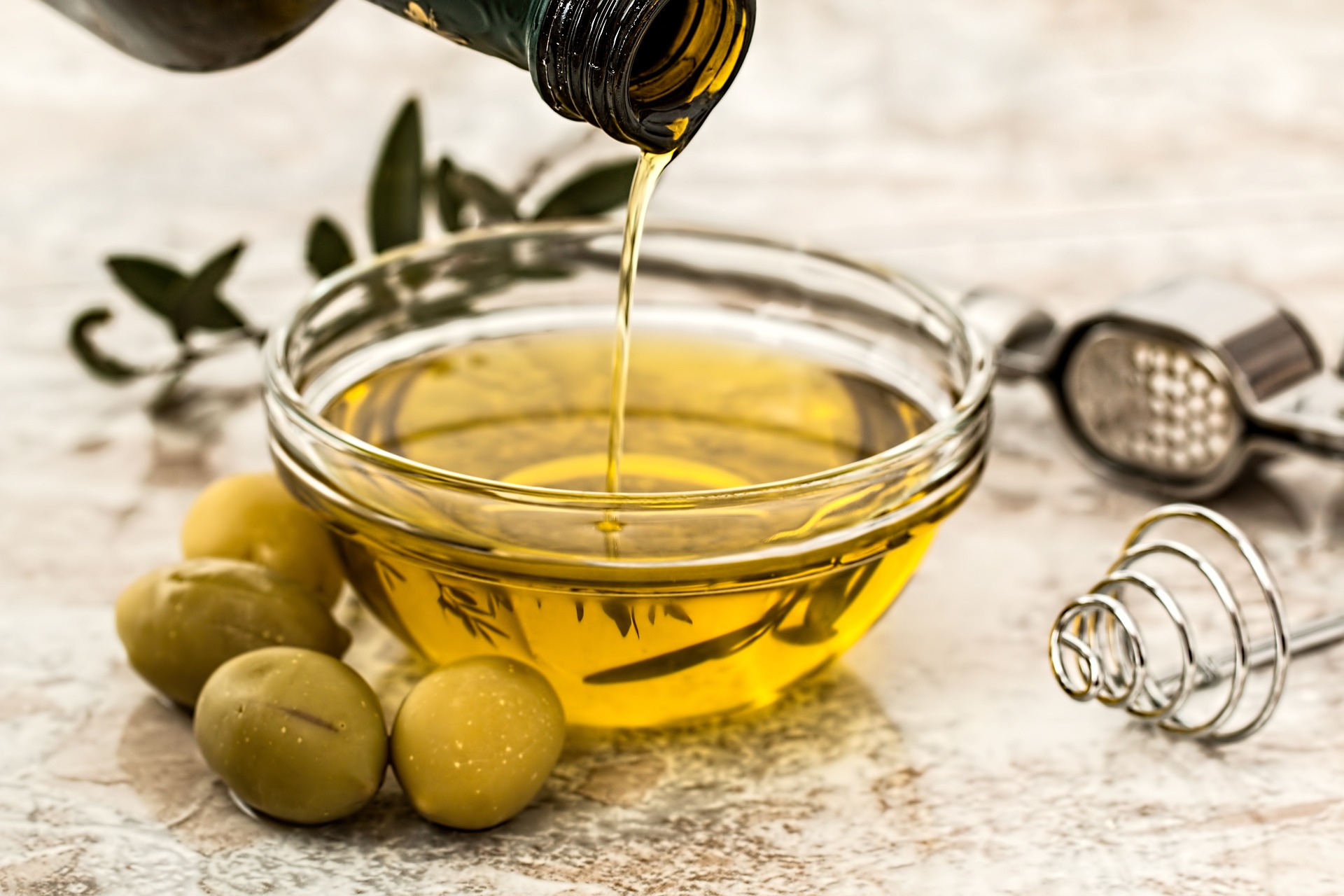 Olive oil pouring into a glass tasting cup, surrounded by olives.